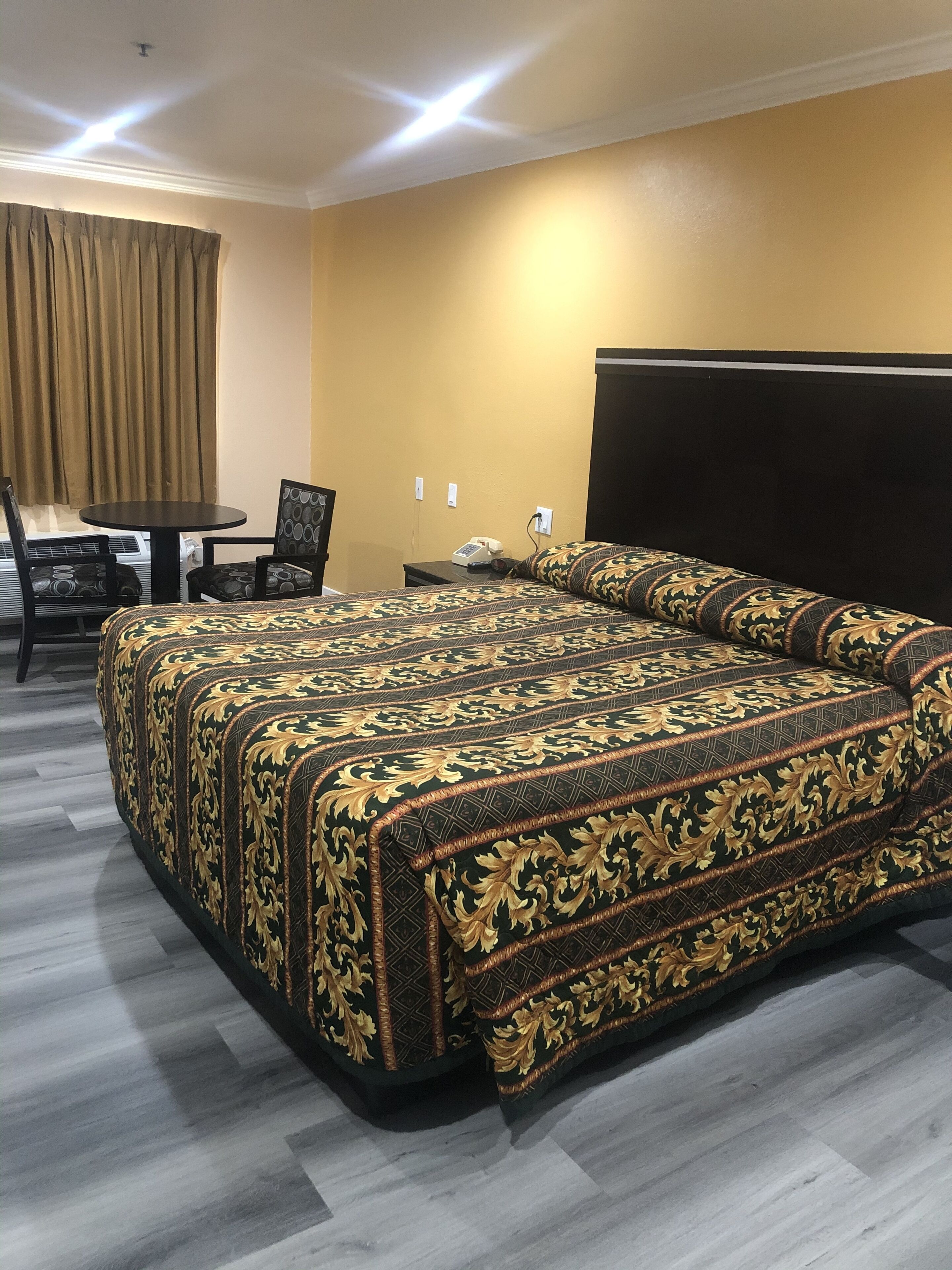 Une chambre d’hôtel avec un grand lit, une table ronde, deux chaises, un téléphone et une tête de lit sombre.