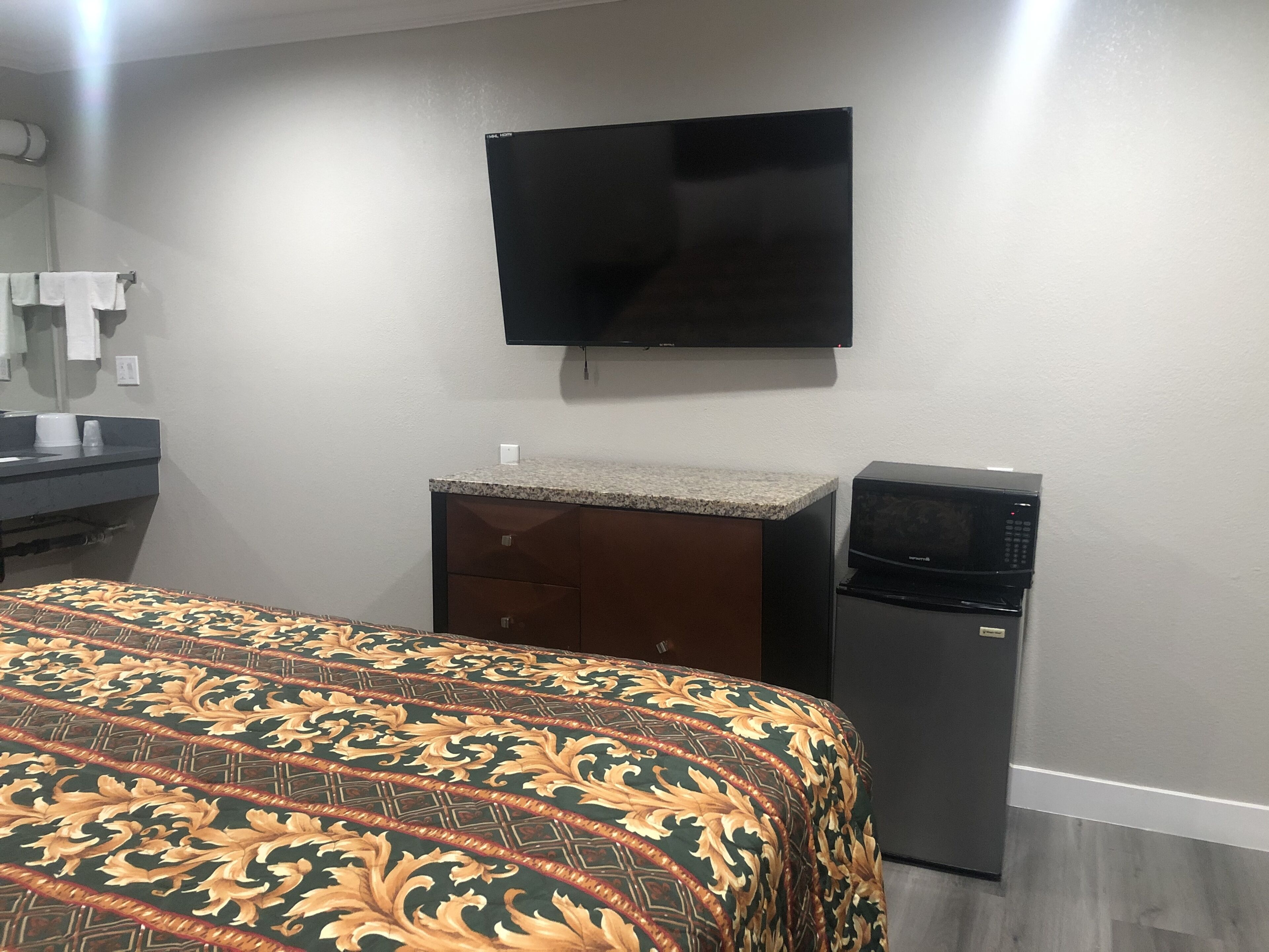 A hotel room with a bed, a TV mounted on the wall, a microwave, and a small refrigerator.