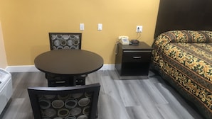 Habitación de hotel con una mesa redonda, una silla, una mesita de noche con un teléfono y una cama con ropa de cama estampada.