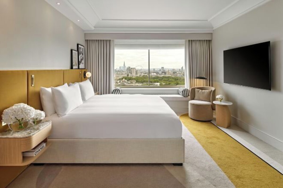 Una habitación de hotel moderna con una cama grande, un televisor de pantalla plana, vista a la ciudad y una pequeña zona de estar.
