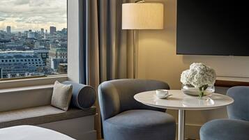 Habitación de hotel con vista a la ciudad, un sofá, una mesa con un florero y un televisor en la pared.