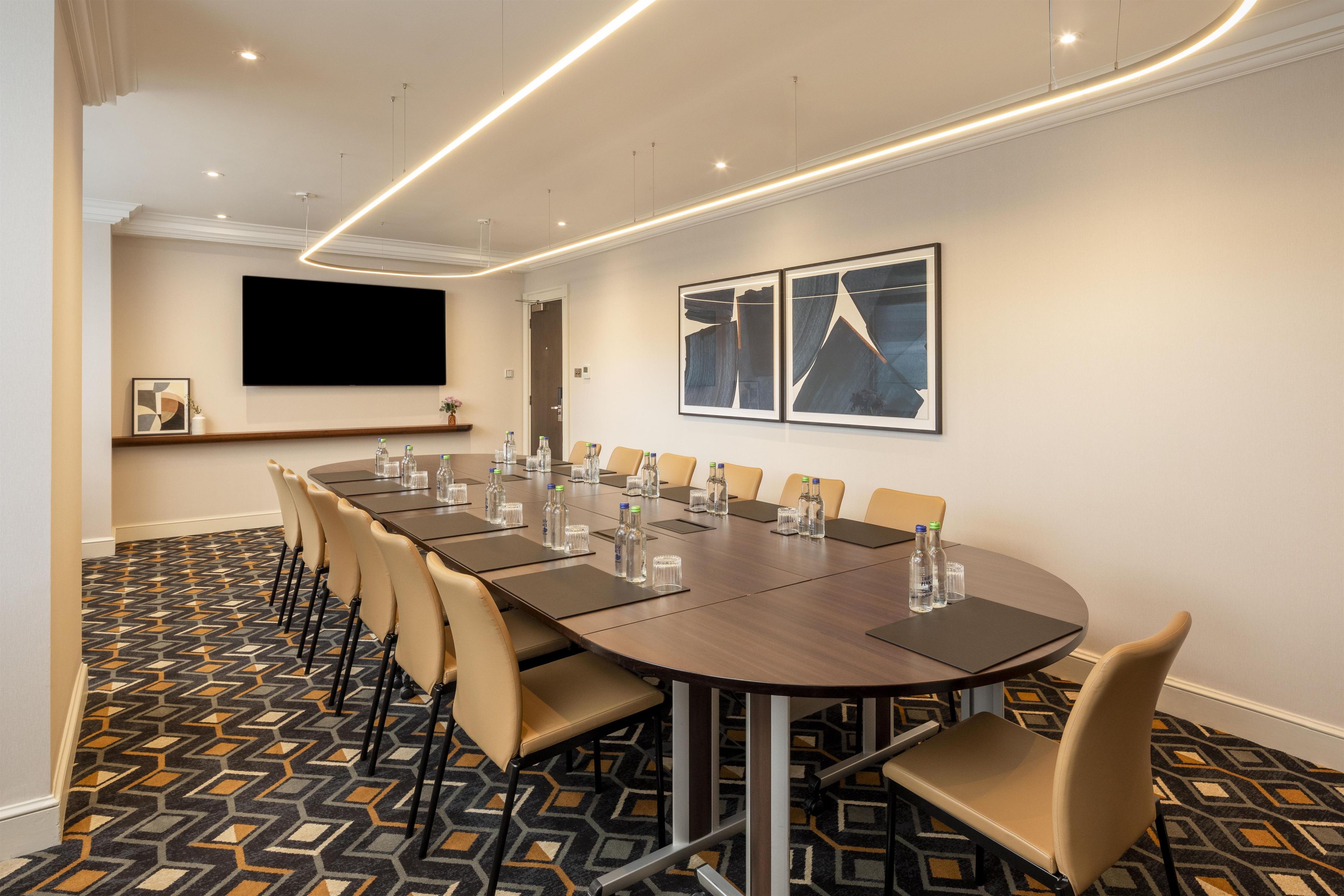 A conference room with a long table, chairs, a projector screen, and framed artwork on the wall.