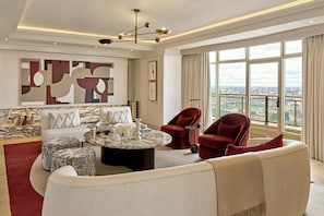 Una sala de estar moderna con una mesa de centro de mármol, sillones de terciopelo rojo, un sofá y vistas a la ciudad a través de grandes ventanales.