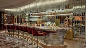 A bar with a curved marble countertop, gold bar stools, and a variety of bottles and glasses. - London Hilton on Park Lane (London)