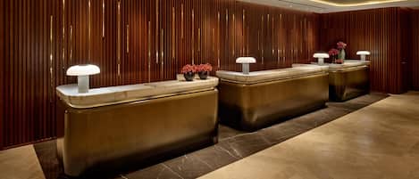 Un área de recepción de diseño moderno, con un panel de madera en la pared, mostradores de mármol y suelo pulido.