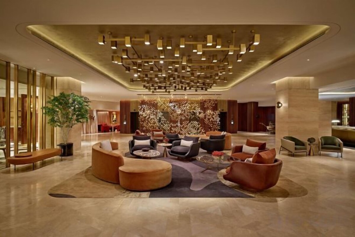 A spacious lobby with a modern chandelier, seating area, and a large decorative wall.