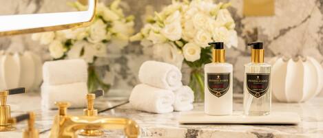 A bathroom vanity with a marble countertop, gold faucets, and two bottles of Penhaligon's Halfeti body lotion and liquid soap.