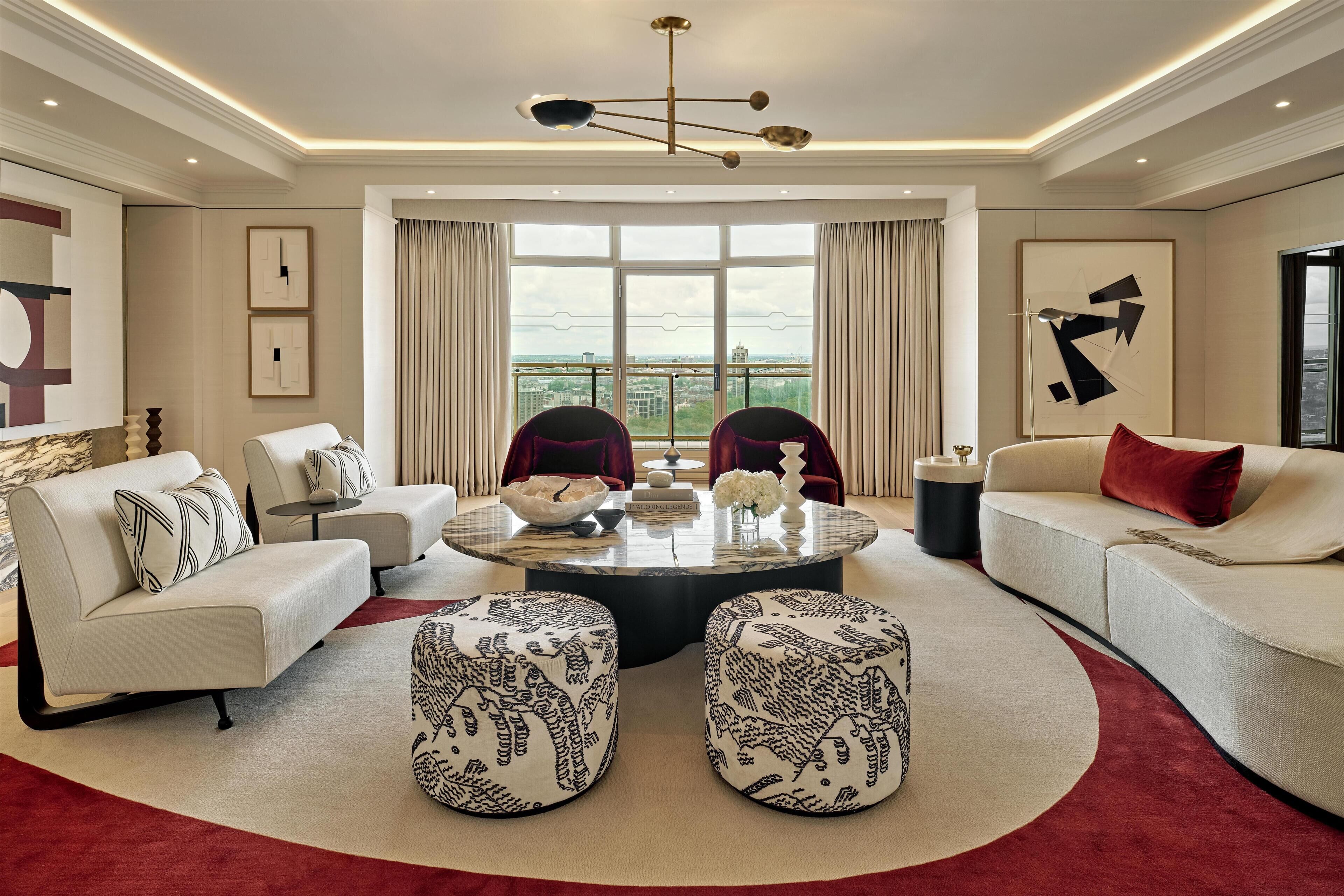 A modern living room with a round coffee table, two sofas, ottomans, and a view of the city through large windows.