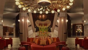 A modern lobby with a red sofa arrangement, a central plant, and a unique ceiling light fixture.