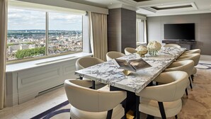 A modern hotel room with a large dining table, comfortable seating, a flat-screen TV, and a city view. - London Hilton on Park Lane (London)