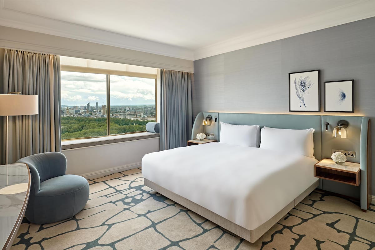 Ett hotellrum med en stor säng, ett skrivbord, en stol, utsikt över stadsbilden och två inramade konstverk på väggen.