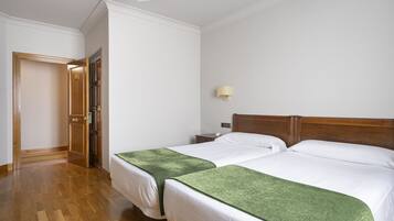 Quarto de hotel com duas camas, cabeceiras de madeira, uma mesa de cabeceira e um abajur fixado na parede.