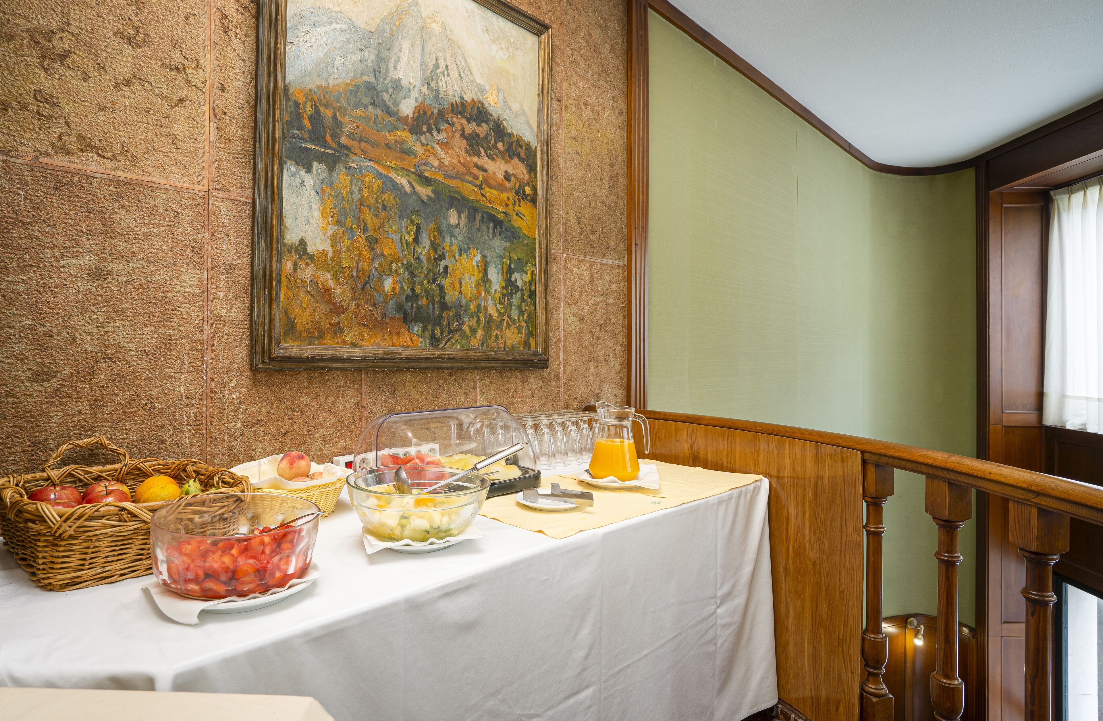 Un bufé de desayuno con diversas frutas y bebidas, un cuadro en la pared y una escalera.