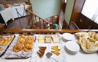Uma mesa de buffet com diversos pães e doces, uma escadaria e uma área de refei ções ao fundo.