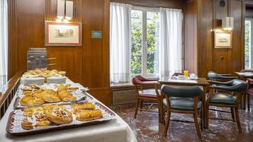 Un bufé de desayuno con pasteles y un comedor con sillas y mesas.