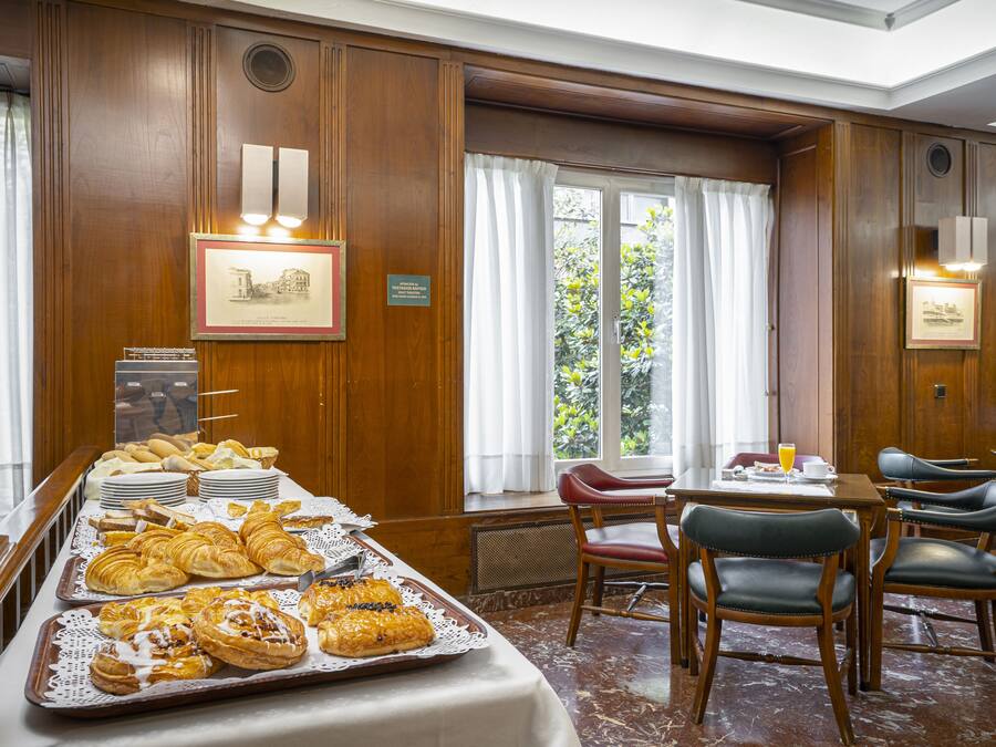Un bufé de desayuno con pasteles y un comedor con sillas y mesas.