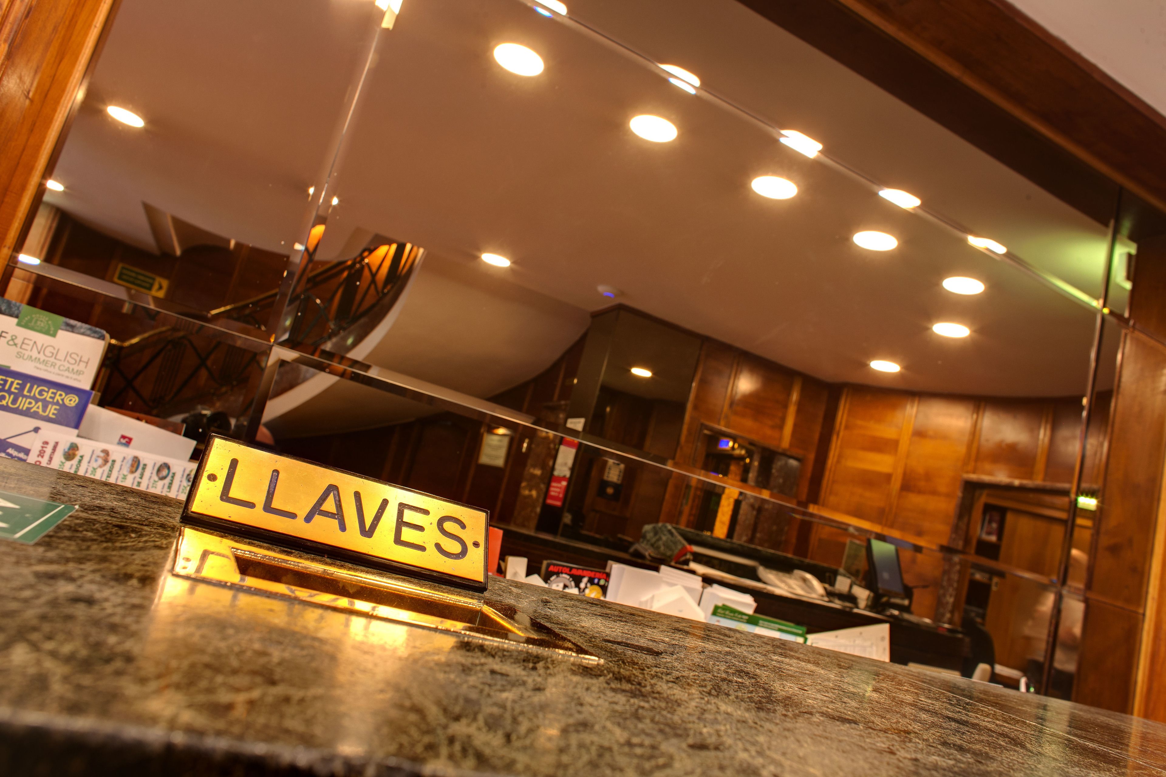A hotel reception area with a marble counter, a sign reading "LLAVES," and a wooden interior.