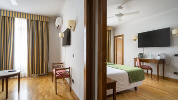 A hotel room with a bed, a desk, a chair, a television, and a ceiling fan.