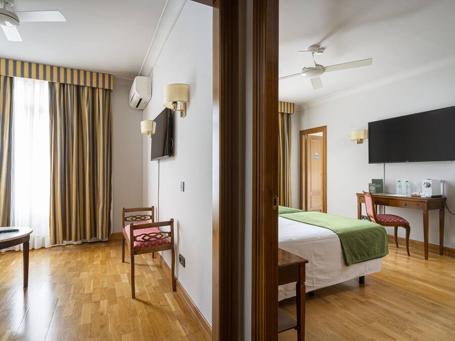 A hotel room with a bed, a desk, a chair, a television, and a ceiling fan.