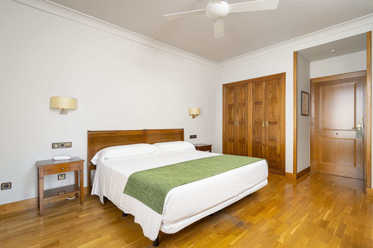 A bedroom with a wooden bed, bedside tables, a ceiling fan, and wooden wardrobes.