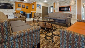 A lobby with patterned sofas, a coffee table, and a TV. There are framed pictures on the wall and a sign about business center rules. - Best Western Airport (Tulsa)