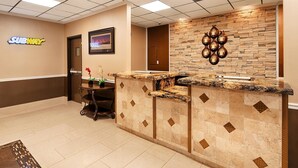 A hotel lobby with a Subway sign, a reception desk with a stone wall, and a framed picture of a cityscape. - Best Western Airport (Tulsa)