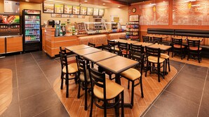 A restaurant interior with multiple tables and chairs, a beverage dispenser, a refrigerator, and a menu board. - Best Western Airport (Tulsa)