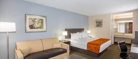 A hotel room with a bed, a sofa, a desk, a chair, and two bedside tables with lamps.
