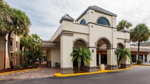 Fachada de hotel en tonos beige, con entradas arqueadas y palmeras.