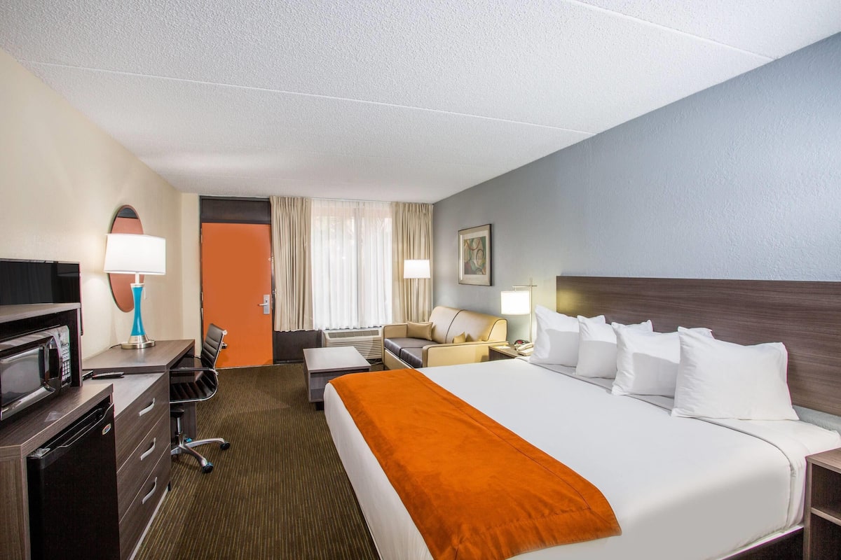Une chambre d’hôtel avec un grand lit, un bureau avec un ordinateur, une chaise, une télévision et une fenêtre avec des rideaux.