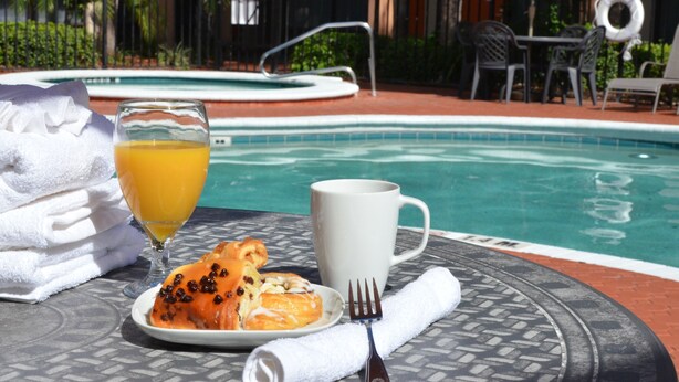 Una mesa de comedor con un plato de comida, un vaso de jugo de naranja, una taza blanca y un tenedor.