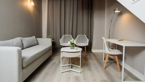 A modern living room with a sofa, two white chairs, a small round table with a vase of flowers, and a desk with a lamp. - SuMa Recoleta Hotel (Buenos Aires)