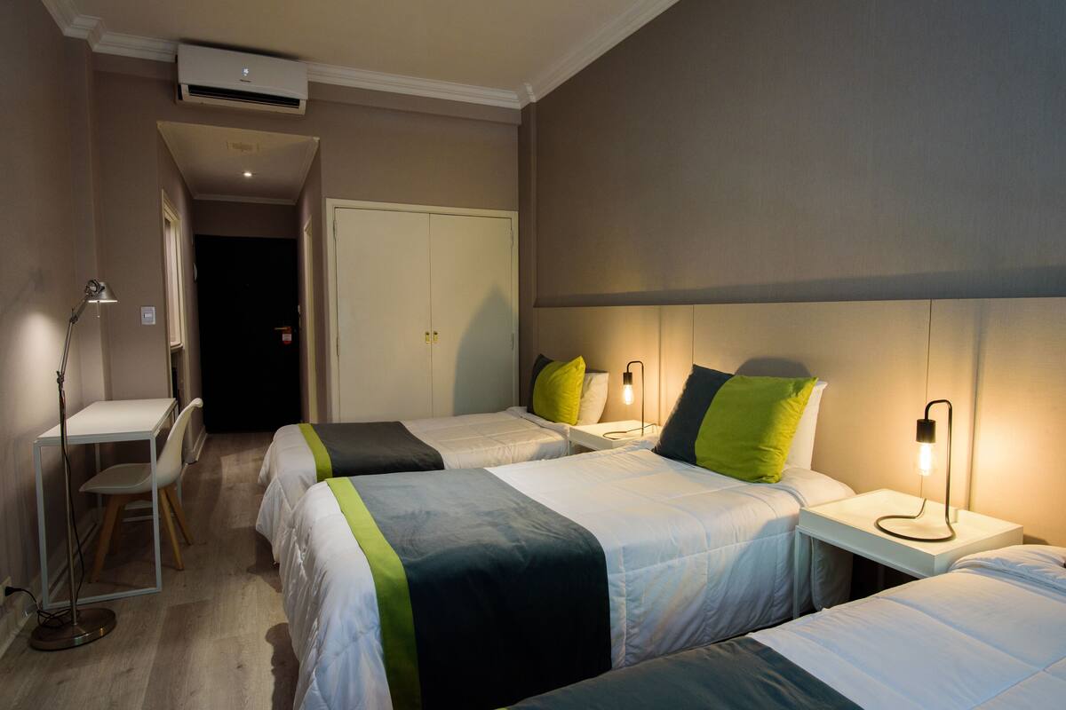 A hotel room with two beds, a desk, and a chair. There is a door leading to another room.