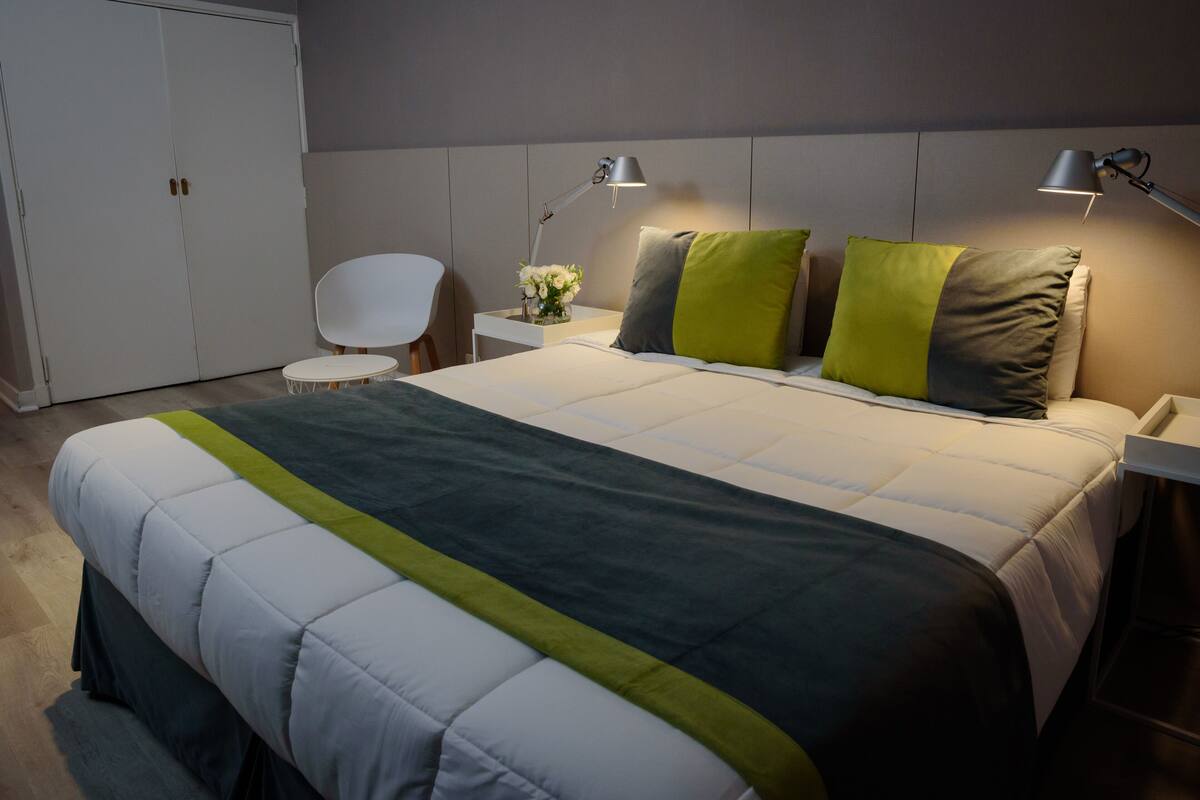 A neatly arranged hotel room with a large bed, two bedside lamps, a small table with a vase of flowers, and a chair.