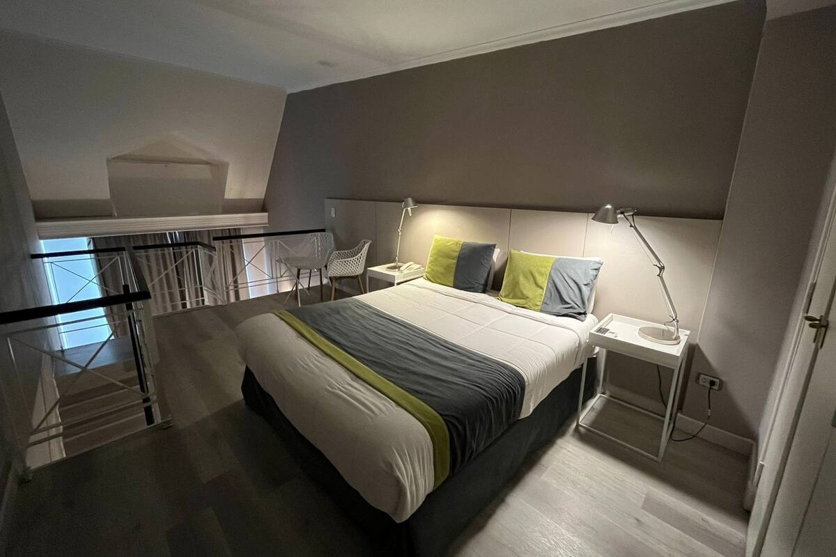 A modern hotel room with a large bed, bedside tables, a desk, and a chair.