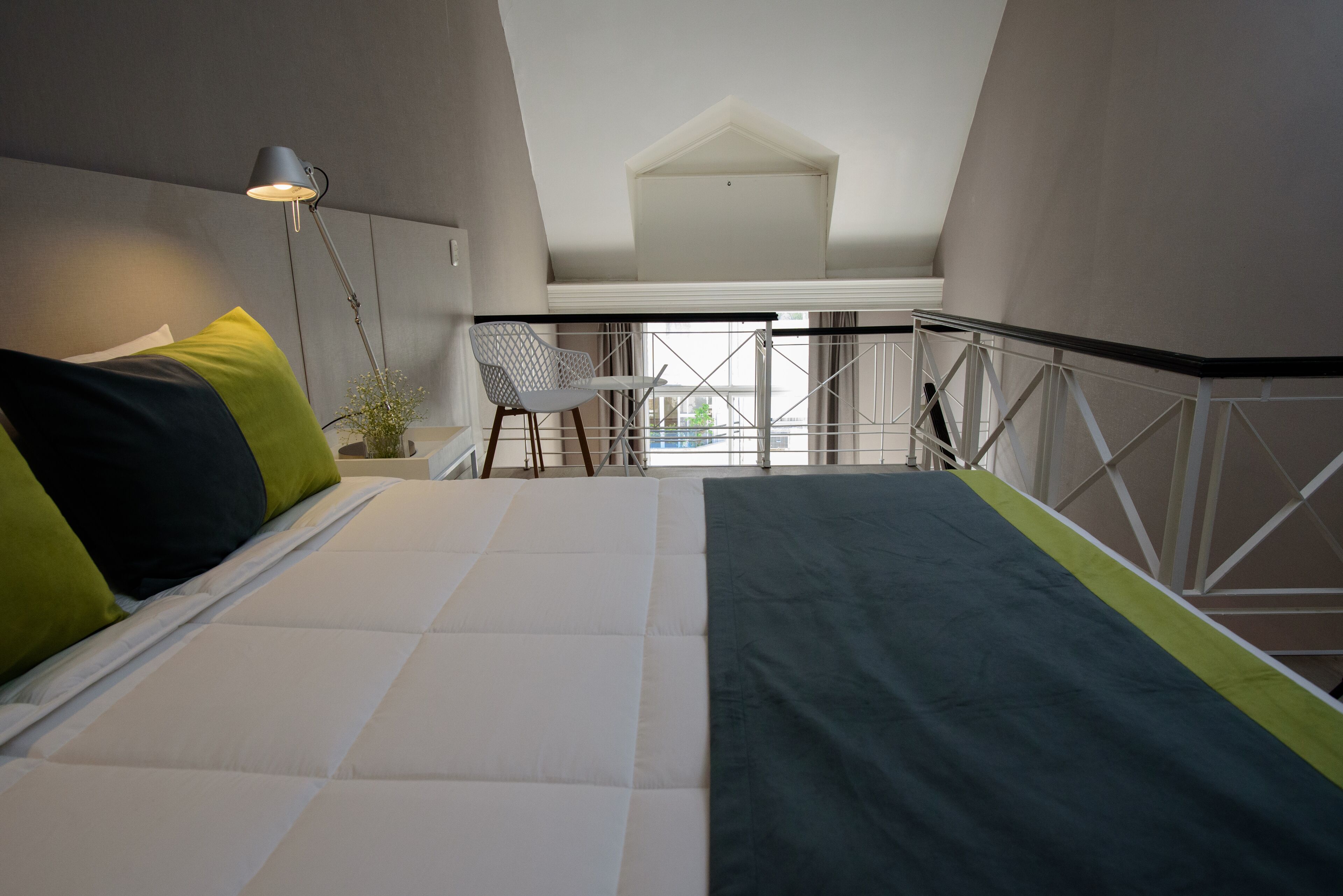 Et soveværelse med seng, stol, skrivebord og en balkon med gelænder.
