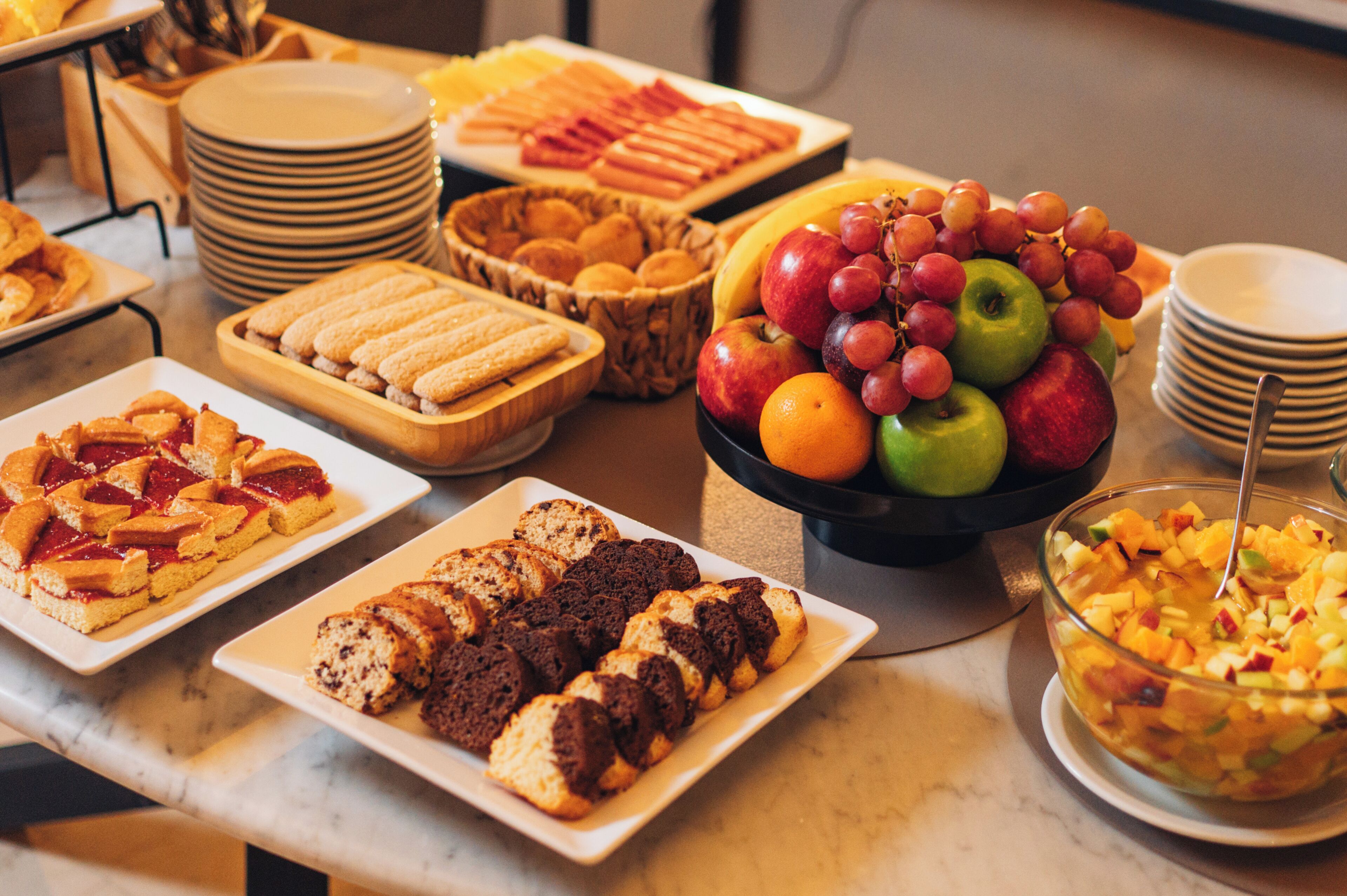 Un bufé con diversos alimentos, incluyendo frutas, pasteles y una ensalada de frutas.