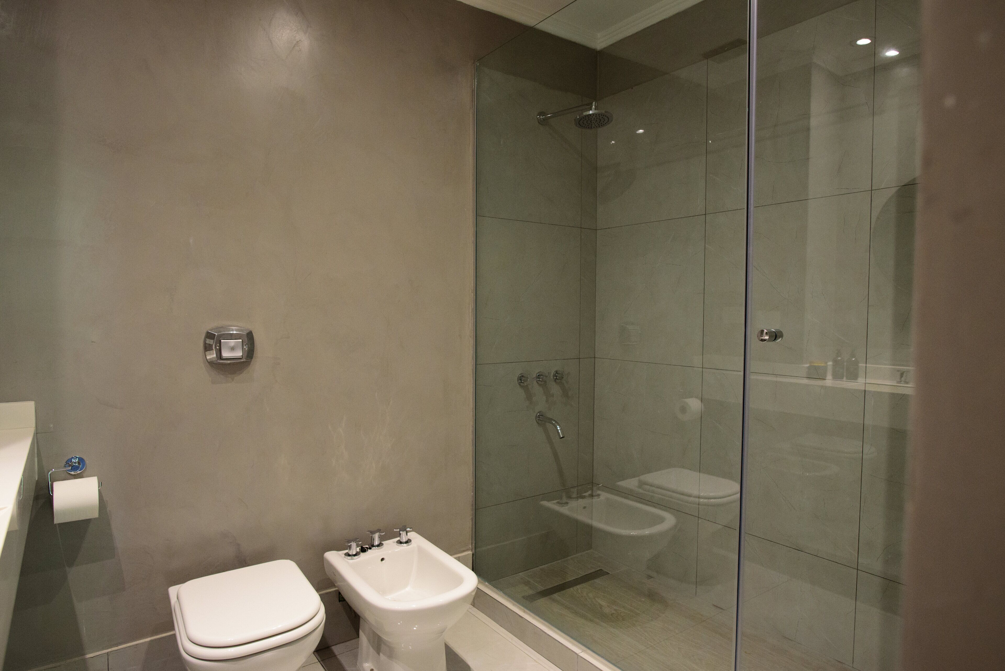 A bathroom with a toilet, bidet, and glass-enclosed shower stall.