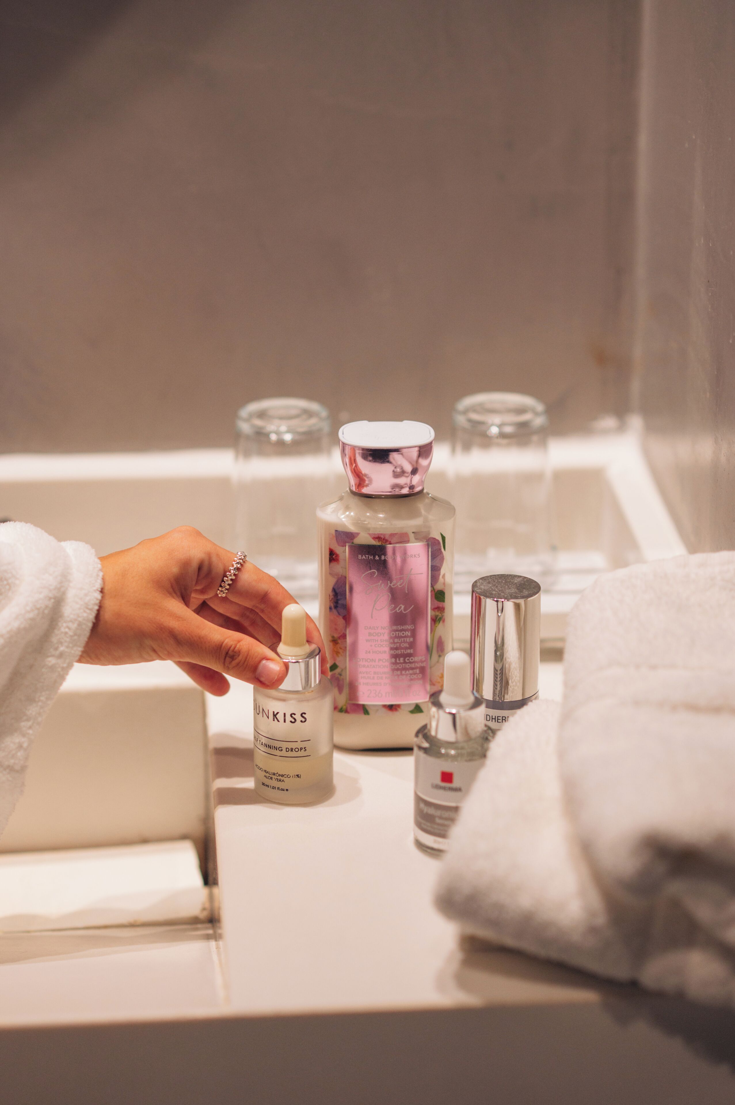 Ein Badezimmer mit einem weißen Waschbecken, Tropfen von Unkiss Tanning, einem Fläschchen Badesalz und einem Glasbehälter.