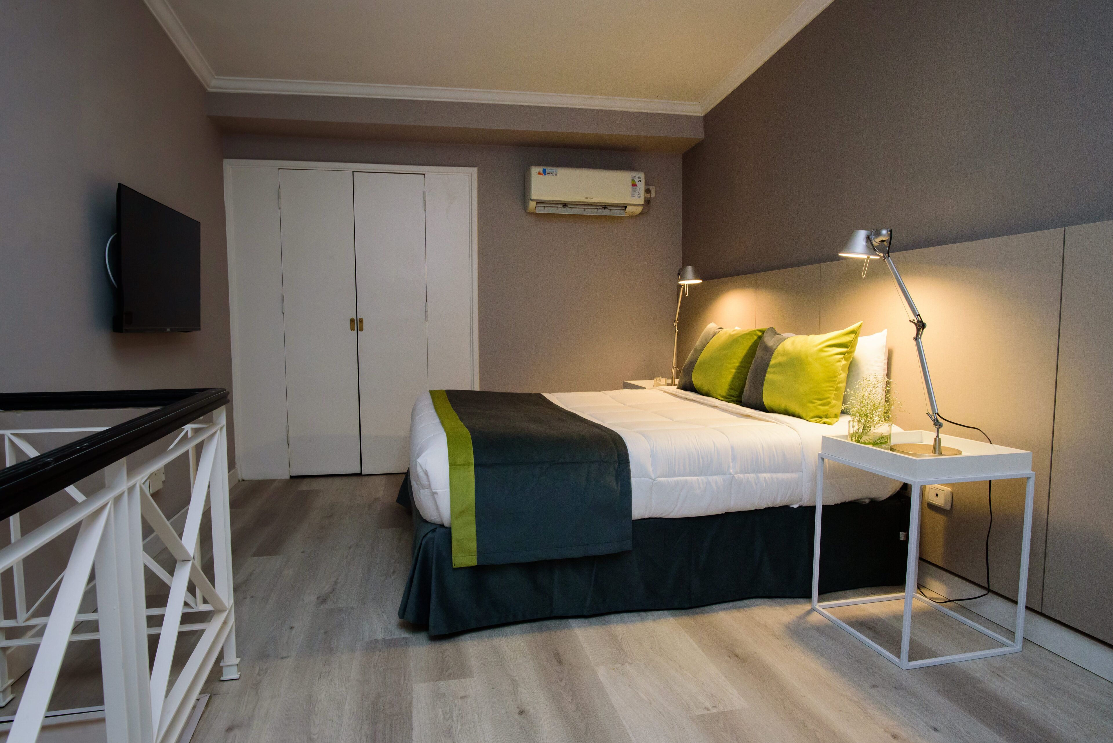 Een slaapkamer met een bed, nachtkastje, lamp, airconditioning en een aan de muur bevestigde televisie.