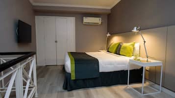 Een slaapkamer met een bed, nachtkastje, lamp, airconditioning en een aan de muur bevestigde televisie.