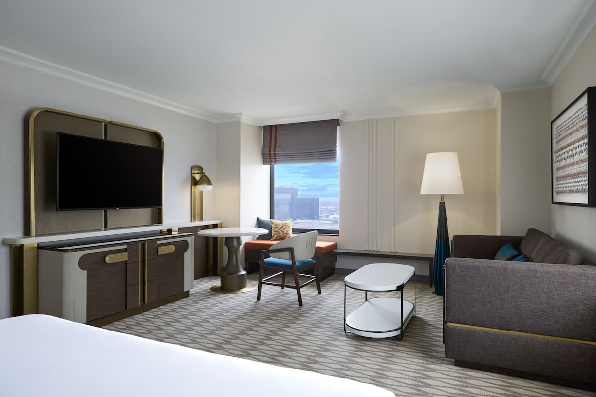 Quarto de hotel com cama, escrivaninha, cadeira, sofá, televisão e janela com vista.