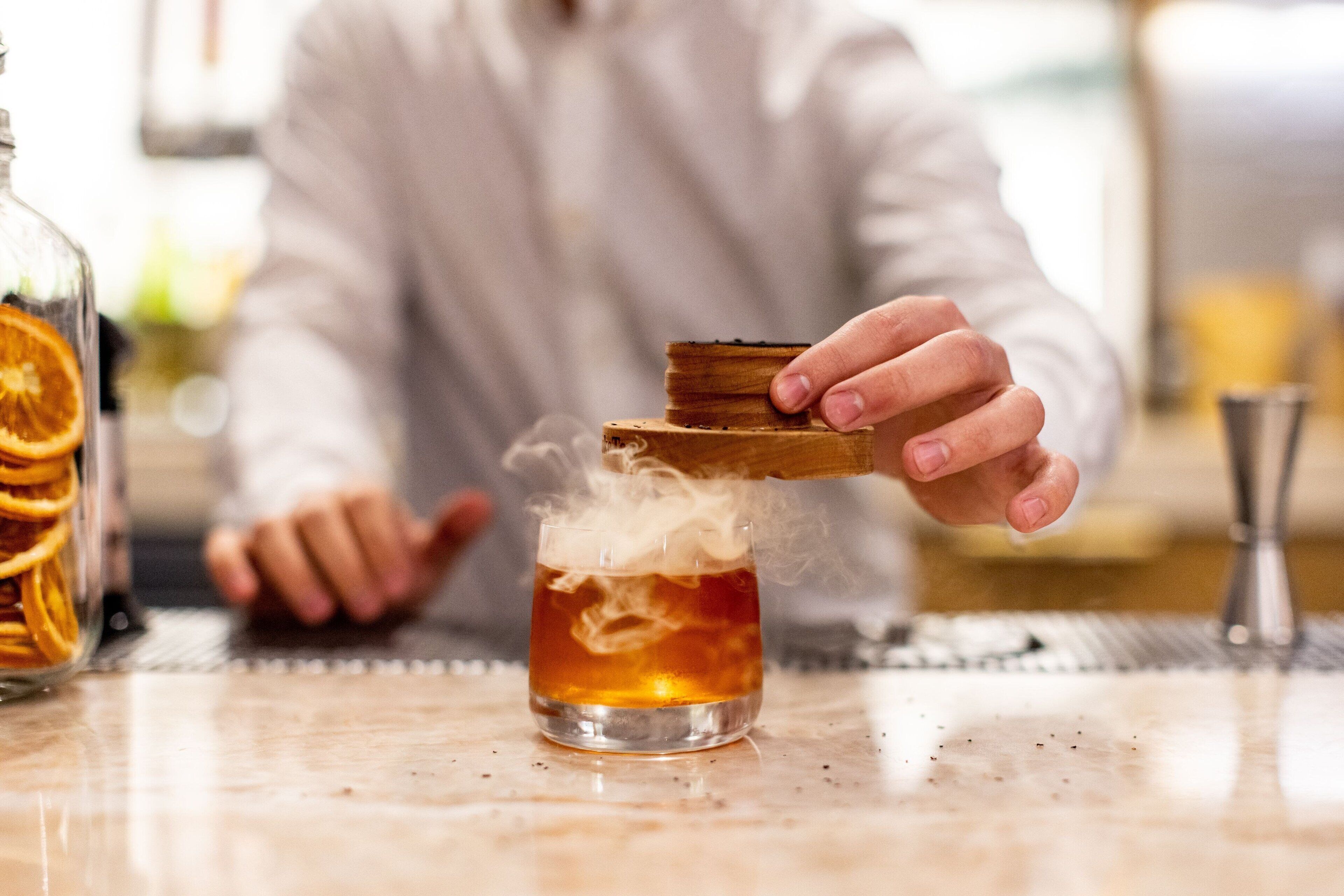Una persona vertiendo una bebida desde un coctelera de madera en un vaso.
