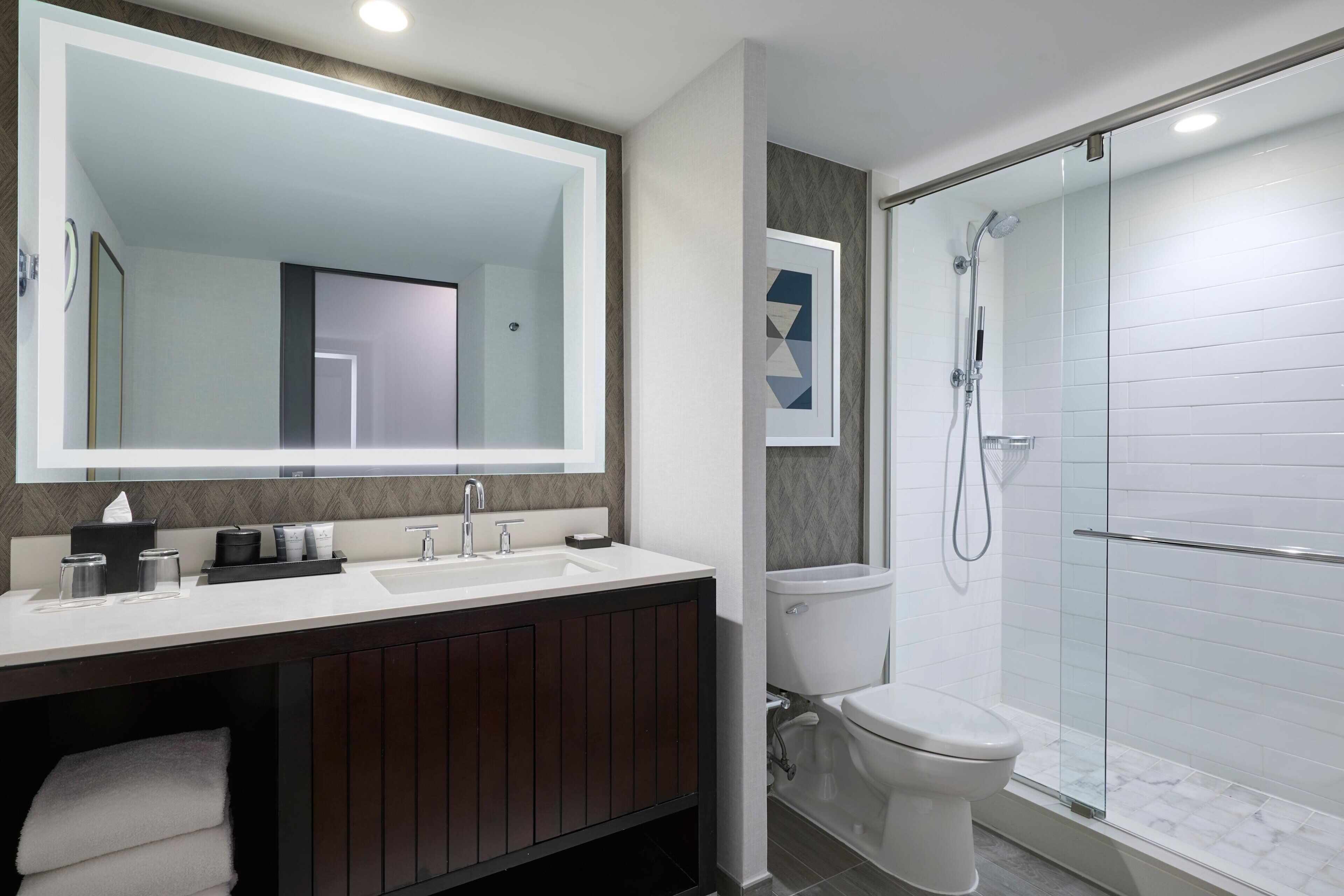 Een moderne badkamer met een grote spiegel, een wastafel, een toilet en een douche met glazen wanden.