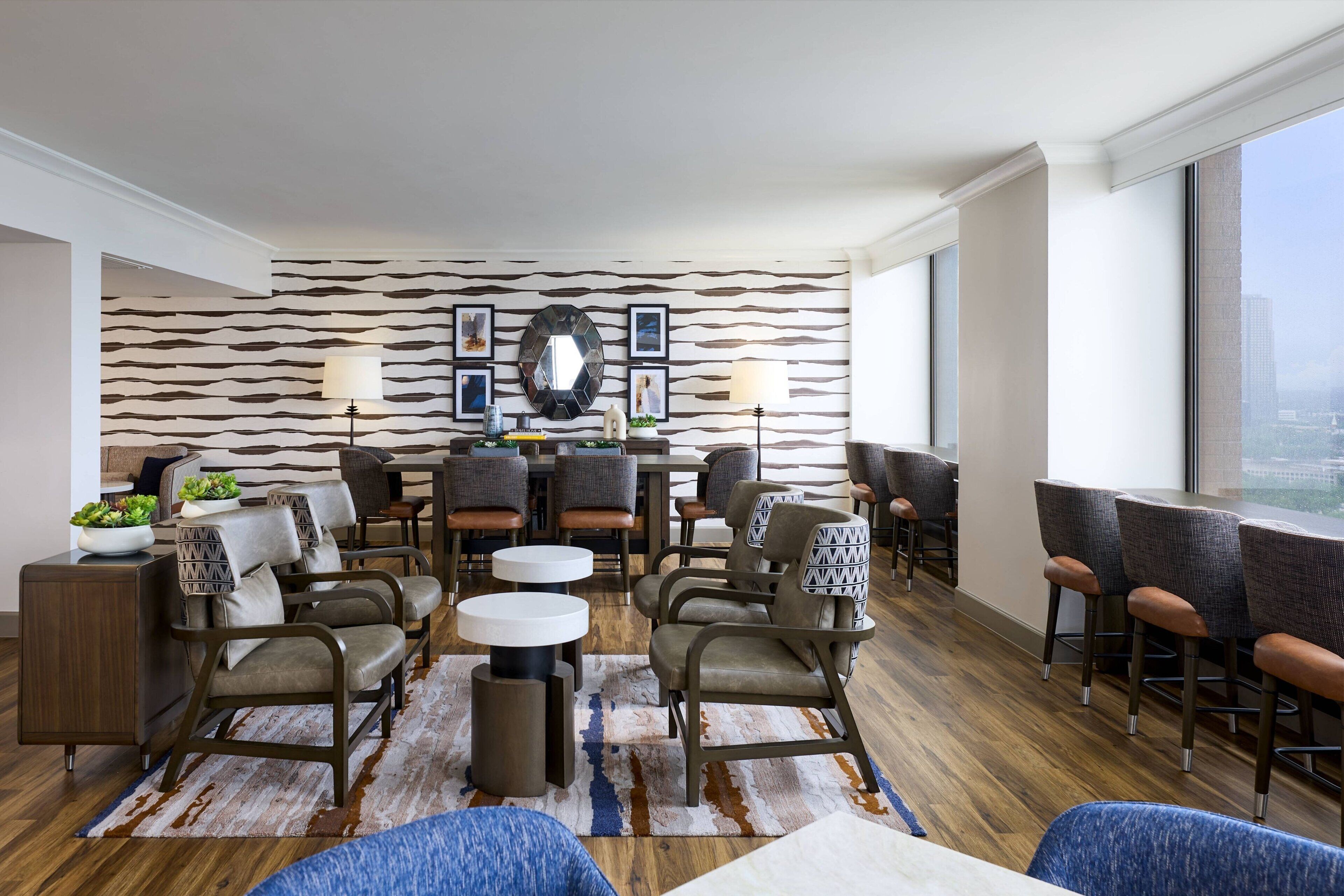 Een moderne zithoek met een behang met patroon, een centrale tafel met stoelen, en een groot raam met uitzicht over de stad.