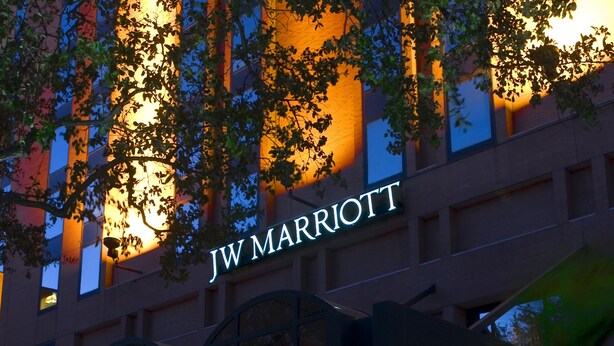 Entrada de um hotel JW Marriott, com acesso coberto, colunas e uma placa sobre as portas.