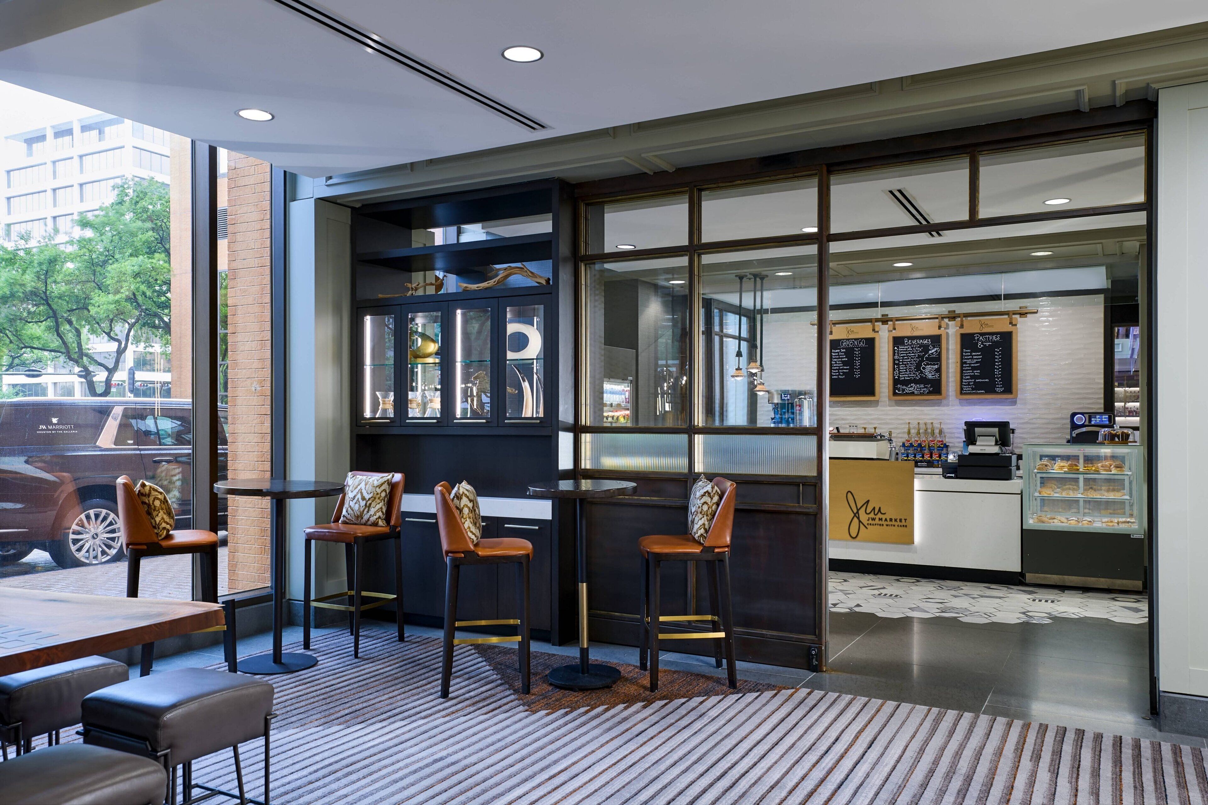 A modern cafe with a glass storefront, bar stools, and a seating area with tables and chairs.