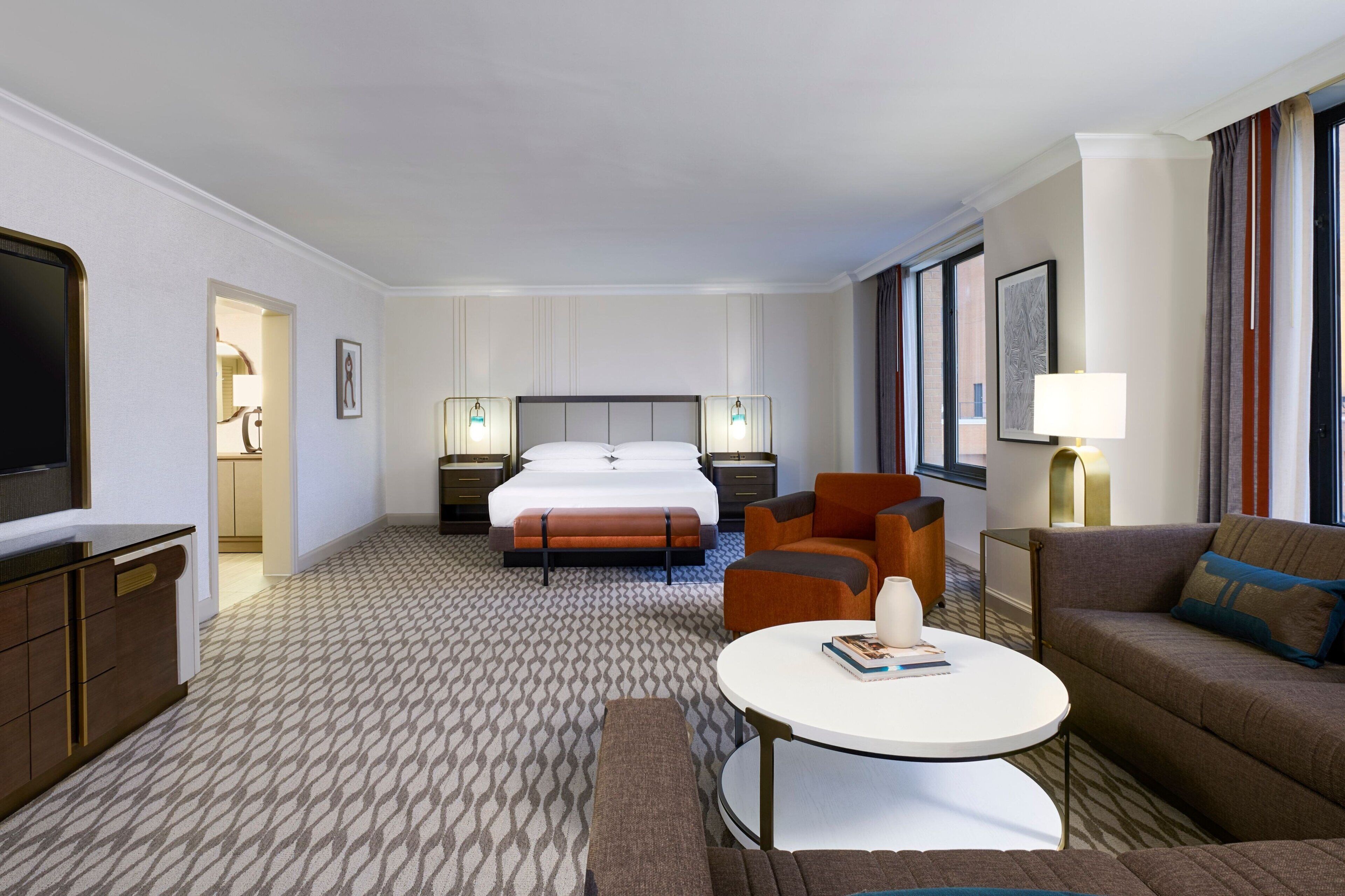 A hotel room with a bed, two armchairs, a sofa, a television, and a small table.