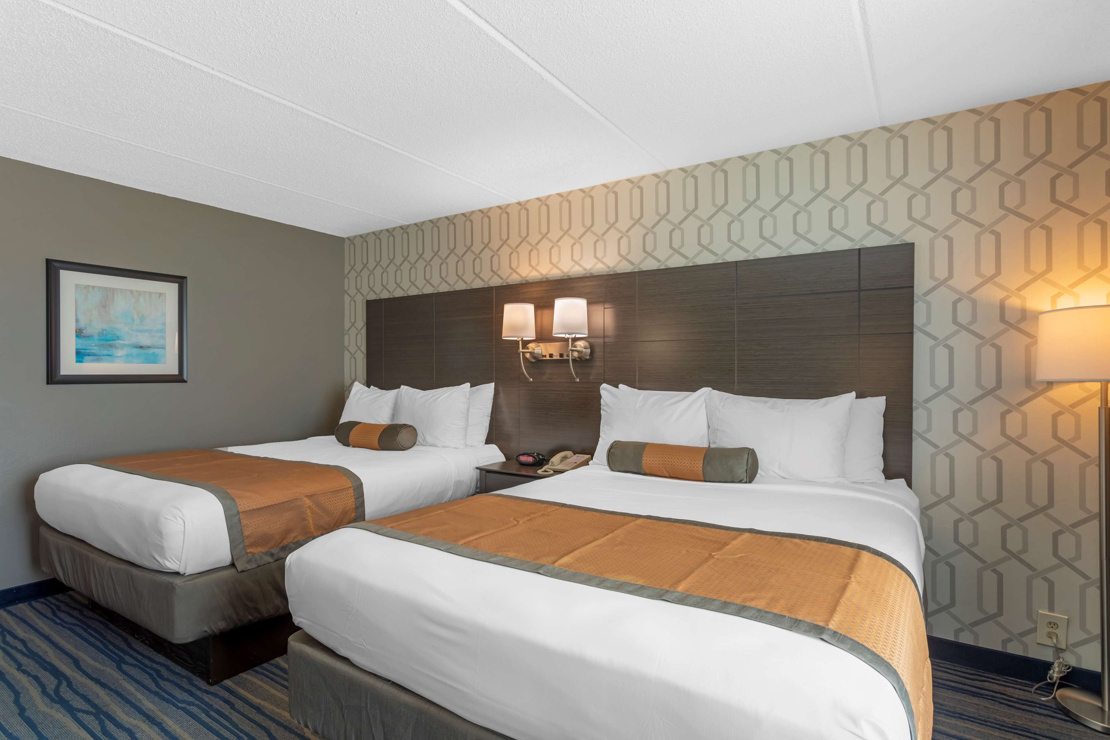A hotel room with two beds, a nightstand, and a wall-mounted lamp.