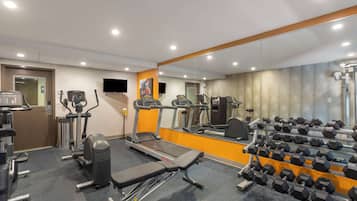 A gym with treadmills, elliptical machines, a bench, and a rack of dumbbells.
